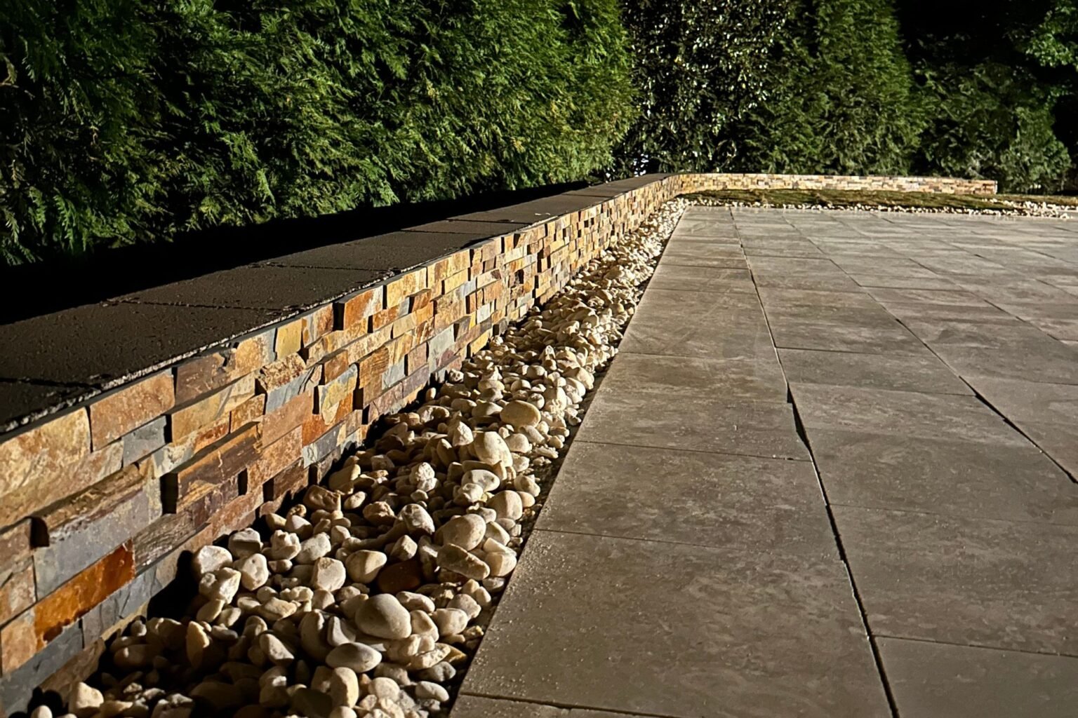 Retaining wall, pavers, and rock border highlighted at night