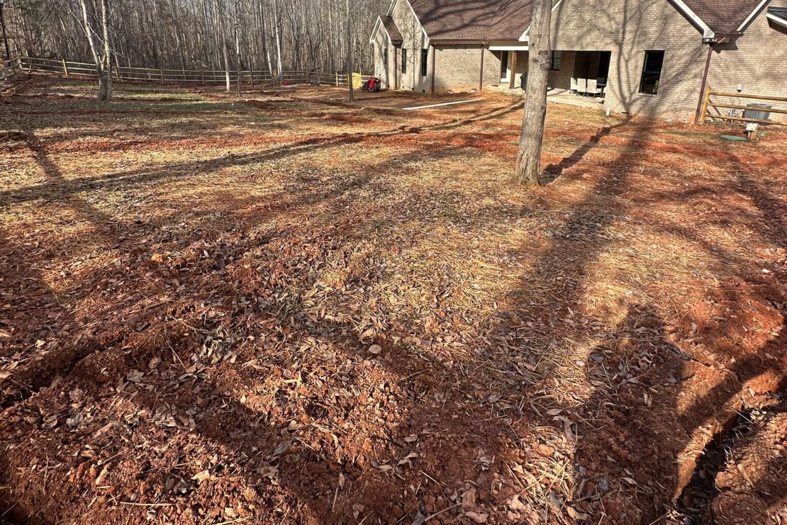 Bare red clay backyard beside a brick house during landscape preparation
