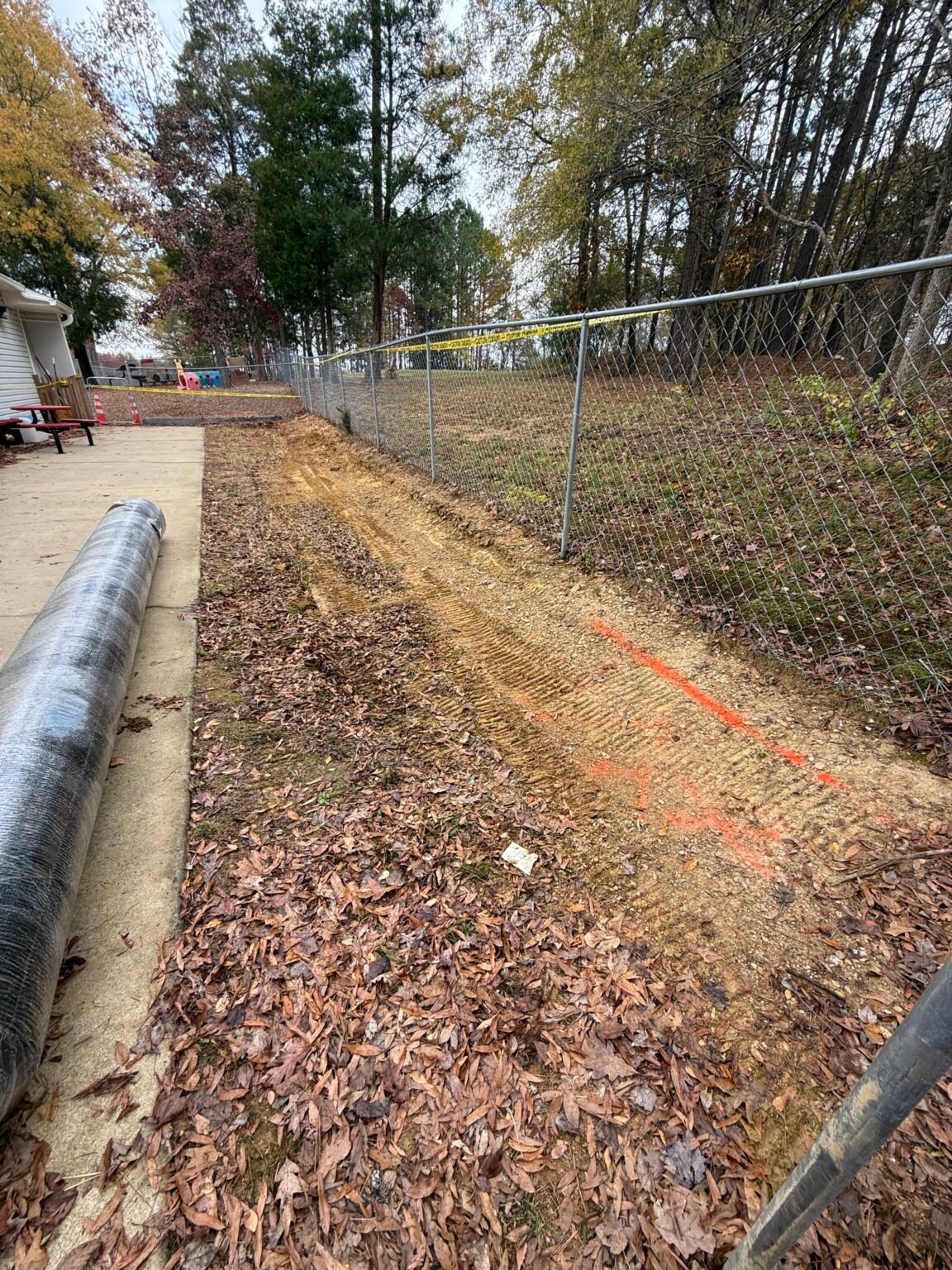 Backyard before renewal with exposed soil, sparse grass, leaves, and chain-link fence