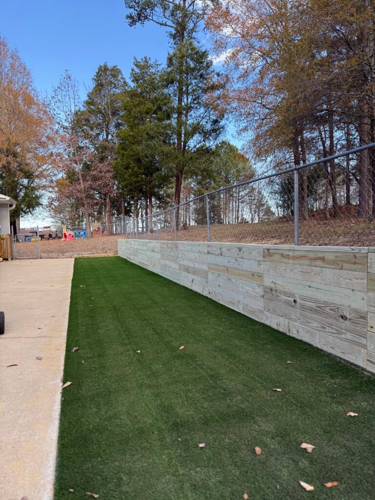 Lush Backyard Transformation – Project 9 Backyard turf strip with a wood retaining wall and fence