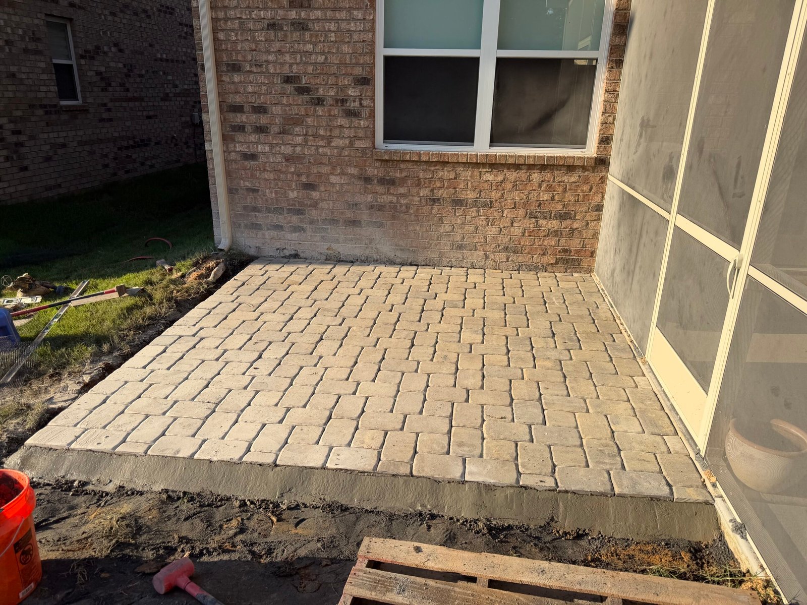 Finished light-toned paver patio viewed beside the brick wall and screened porch entry