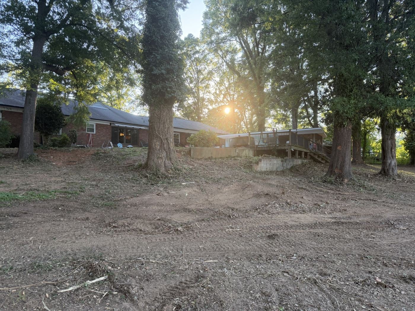 Opened-up backyard below the house and deck with mature trees remaining