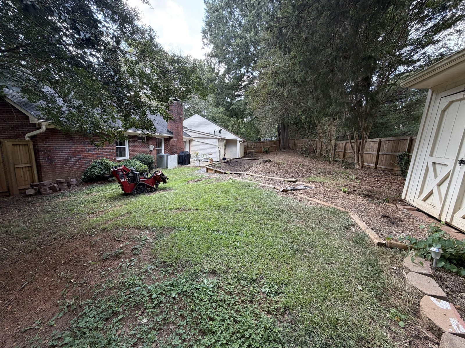 Original backyard with patchy grass, a timber-edged area and stump-grinding equipment