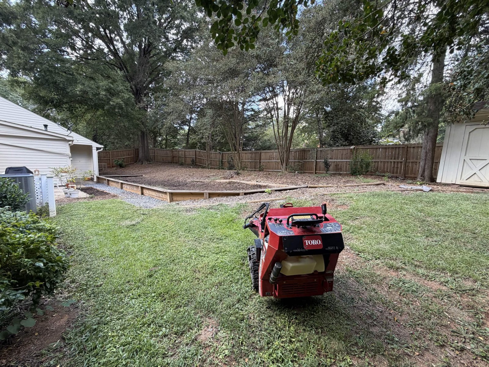 Stump grinder on site beside the original timber-edged backyard area