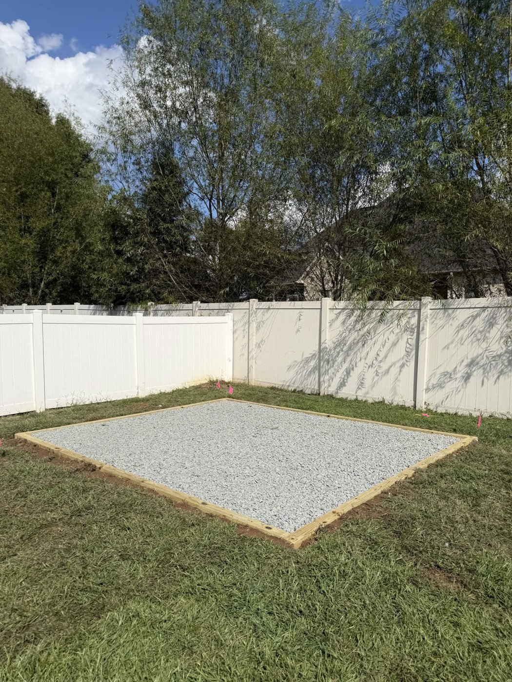 Finished gravel pad viewed toward the white fence and trees