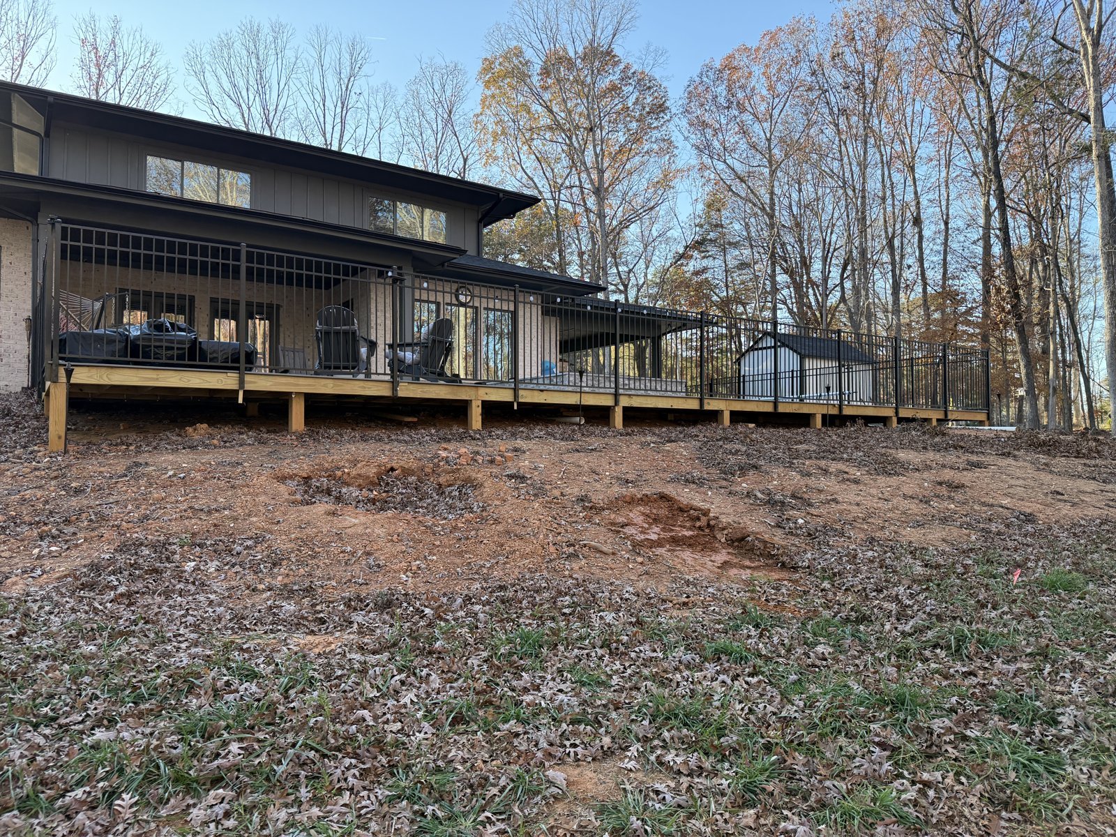 Sloping ground and fallen leaves below the deck before the retaining wall was installed